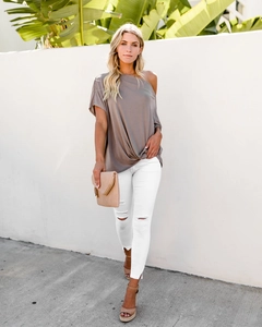 Detail of taupe one-shoulder loose top paired with white ripped skinny jeans for summer