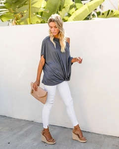 Outdoor shot of a women's dark grey off-shoulder top paired with white ripped denim jeans