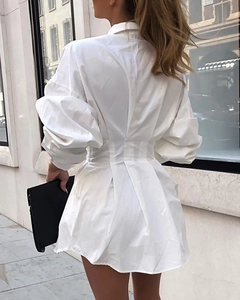 Détail d'une robe chemise blanche à manches longues avec taille cintrée et jupe plissée