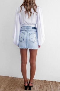 Dettaglio minigonna in denim con orlo a vivo, tasche decorative e etichetta in pelle sul retro