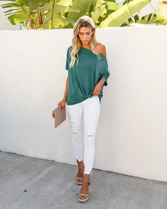 Outdoor street style view of woman in off-shoulder dark green top and white ripped jeans