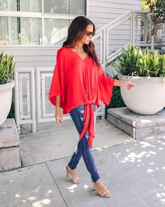 Detail of red V-neck blouse featuring flutter sleeves and a stylish waist tie-knot design