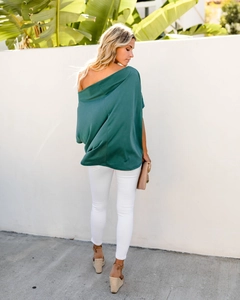 Back view of a loose dark green off-shoulder top and white slim pants in outdoor light