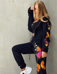 Detail of black tracksuit showing vibrant orange gradient butterfly prints on sleeves and legs