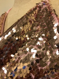 Detail of rose gold sequins sewn on pink mesh fabric for a shimmering party dress