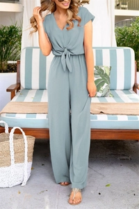 Detail view of v-neck blue-grey wide leg jumpsuit with waist tie in a resort setting
