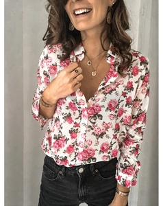 Détails du motif de roses roses sur un chemisier blanc à manches longues avec bijoux dorés