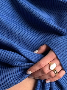 Detailed shot of gold stacked rings with oval stone inlay on navy ribbed knit fabric