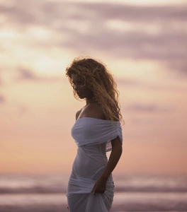 Detail of off-the-shoulder white pleated maxi dress against a beach sunset background
