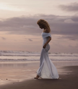 Detail of elegant white off-shoulder mesh maxi dress against beach sunset