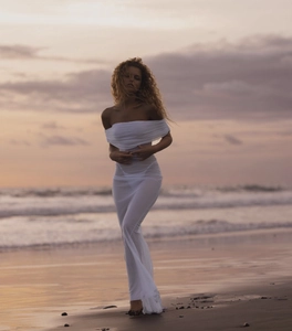 Detail view of white off-the-shoulder mesh dress against a beach sunset backdrop
