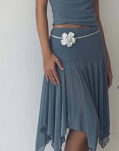 Détail d'une jupe plissée bleu-gris avec ceinture à fleurs 3D et ourlet asymétrique