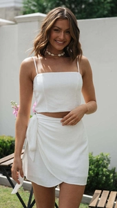 Detail of white two-piece set featuring thin strap crop top and side tie wrap mini skirt