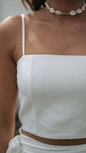 Detail of white cotton linen crop top and lace-up skirt with shell necklace