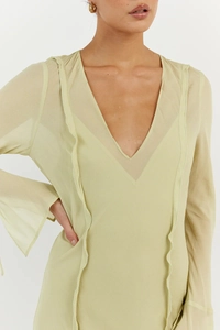 Close-up of a light green V-neck dress featuring delicate ruffle trim and sheer mesh sleeves