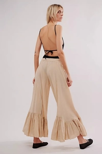 Detail view of beige wide-leg pants with elegant ruffled hem and backless black top