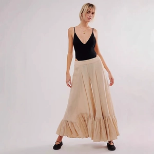 Detail of high-waist beige wide-leg trousers featuring layered ruffle hems and flowing fabric