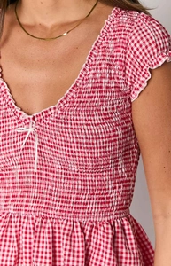 Detail of red gingham smocked fabric with a small white ribbon bow and ruffled edges