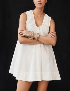 Detailed view of white sleeveless dress featuring a deep V-neckline and pleated trim texture