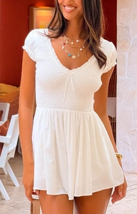 Close-up of white smocked v-neck romper with ruffled neckline and elastic puff sleeves