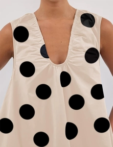 Detailed view of the deep V-neckline with pleated edges on a beige polka dot dress