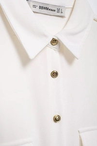 Dettaglio del colletto della camicia bianca con etichetta e bottoni dorati goffrati su crepon