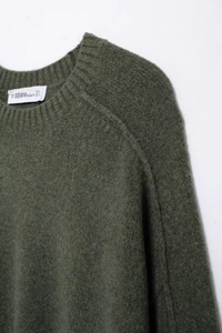 Gros plan détaillé du col du pull en tricot vert foncé avec étiquette de taille S blanche