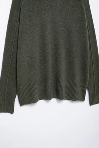 Détail d'un pull en maille olive foncé montrant les poignets et la texture du tissu