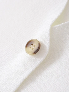 Macro di un bottone in resina marrone su tessuto a maglia bianca del gilet donna a V