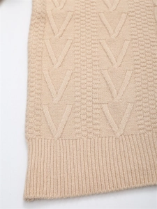 Dettaglio della trama a trecce beige e dell'orlo a costine del maglione in maglia