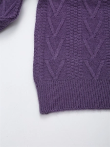 Dettaglio macro di un maglione viola scuro con lavorazione a treccia e bordo a coste