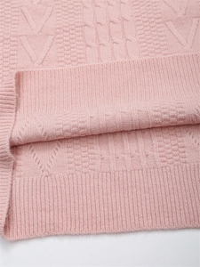 Dettaglio di un maglione rosa in maglia con motivi a treccia e morbida trama a costine