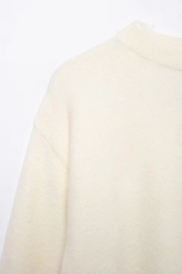 Détail du col rond et de l'épaule tombante sur un pull en maille douce blanc cassé