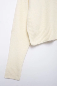 Détail des poignets et de l'ourlet en maille côtelée d'un pull blanc cassé minimaliste