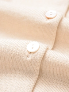 Vista macro della maglia in cashmere beige chiaro con texture fine e bottoni bianchi