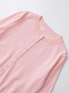 Close-up of crew neck knit cardigan with white buttons in soft pink textured fabric