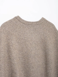 Detailed close-up of textured oatmeal knit fabric and ribbed crew neck of the cape coat