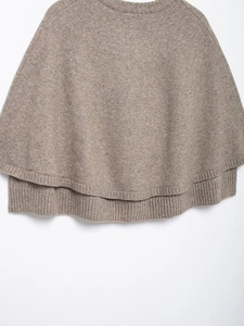 Detailed view of tan knit cape with crew neck and ribbed hem on a clean white background