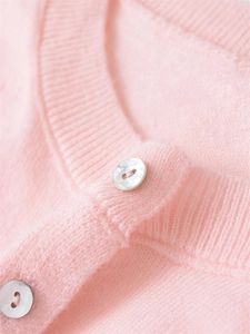 Close-up of pink knit cardigan showing soft texture, ribbed neckline and pearl buttons