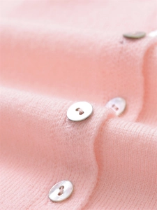 Macro detail of soft pink knit fabric and elegant white pearlescent buttons on cardigan