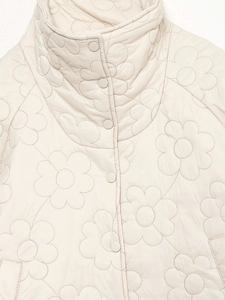 Detailaufnahme der cremefarbenen Winterjacke mit Blumensteppung und praktischen Druckknöpfen