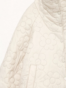 Nahaufnahme des eleganten Blumensteppmusters und der Druckknöpfe an der weißen Steppjacke