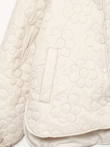 Detail der Blumensteppung und matten Druckknöpfe an einer warmen cremefarbenen Winterjacke