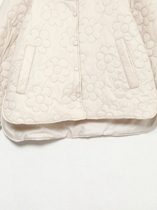 Detail einer gesteppten Jacke mit Blumenmuster, Druckknöpfen und rundem Saumdesign