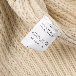 Détail de l'étiquette d'entretien sur pull en maille beige, 65% coton et 35% polyester