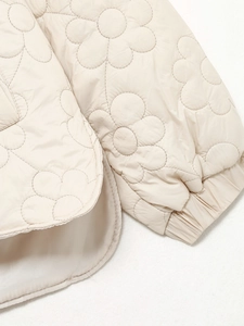 Detail der Blumensteppung und elastische Bündchen am cremefarbenen Damen-Wintermantel