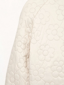 Detailansicht der eleganten Blumensteppung auf der cremefarbenen Winterjacke für Damen