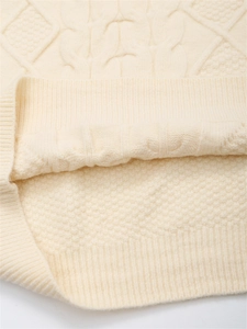 Nahaufnahme von beigem Strickpullover mit Zopfmuster und dicker Wolltextur im Detail