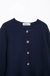 Detail of navy knit cardigan featuring silver embossed buttons and collar brand label