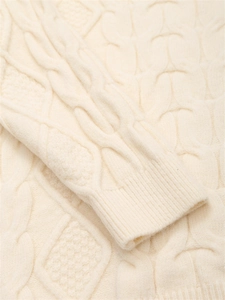 Nahaufnahme von Zopfmustern und Rippbündchen an einem cremeweißen weichen Pullover